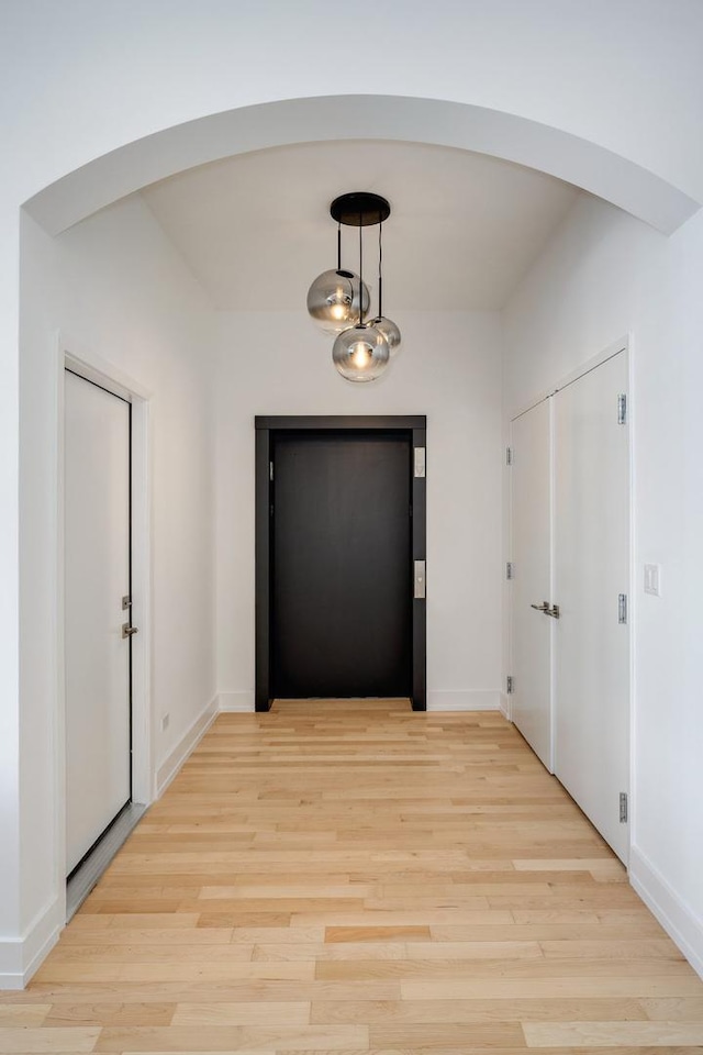 interior space featuring light wood-style floors, baseboards, and arched walkways