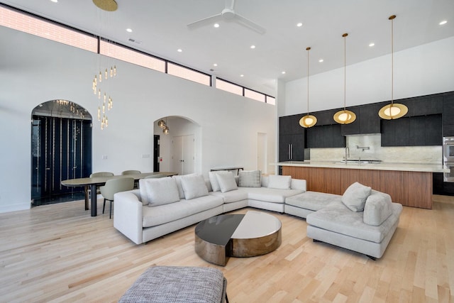 living area featuring arched walkways, a ceiling fan, a towering ceiling, light wood-style floors, and recessed lighting