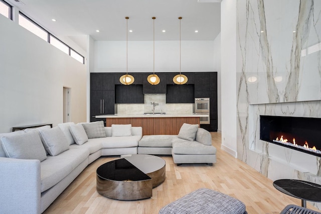 living room featuring a high end fireplace, light wood-style flooring, a towering ceiling, and recessed lighting