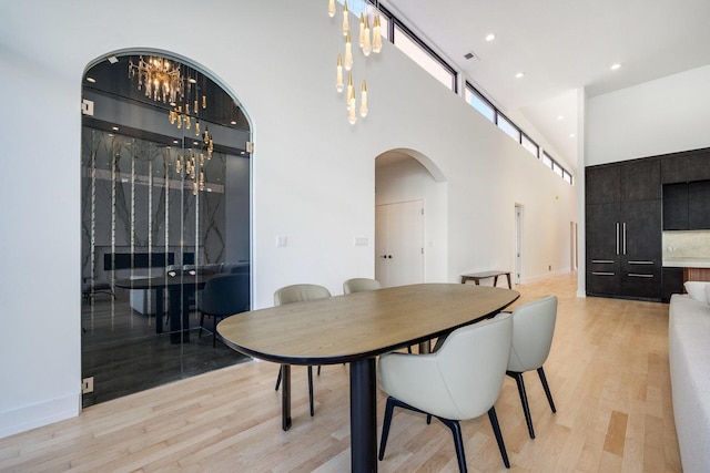 dining area featuring arched walkways, recessed lighting, visible vents, a towering ceiling, and light wood-style floors