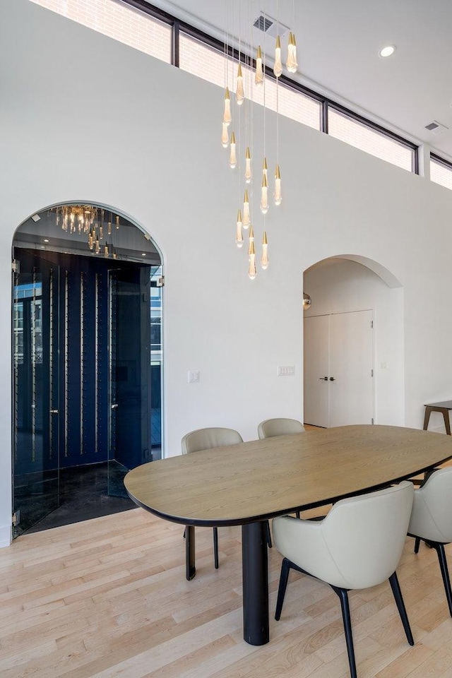 dining area featuring arched walkways, a high ceiling, wood finished floors, and recessed lighting