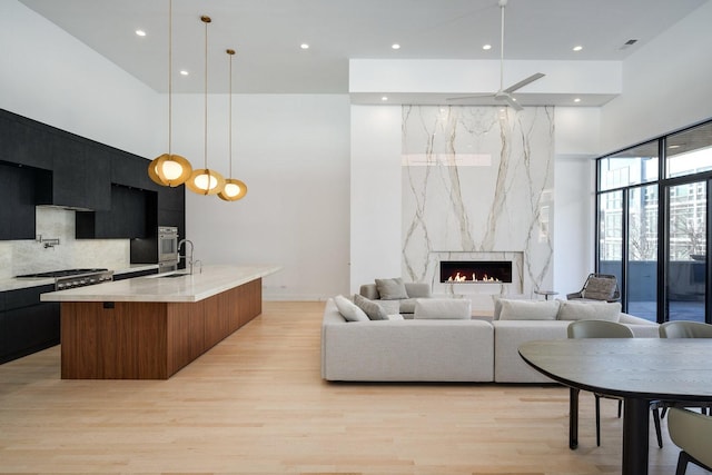 living room with light wood finished floors, a high ceiling, a high end fireplace, and recessed lighting