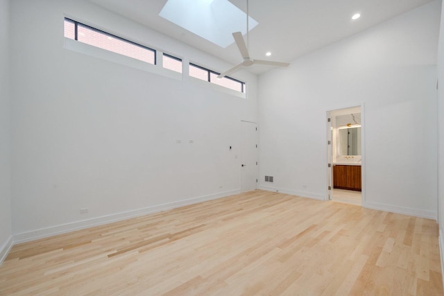 empty room with a wealth of natural light, a skylight, baseboards, and light wood finished floors