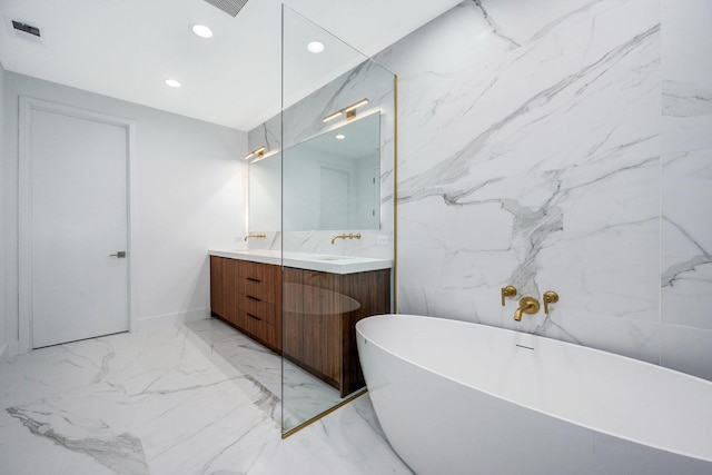 bathroom featuring marble finish floor, double vanity, recessed lighting, a freestanding bath, and stone wall