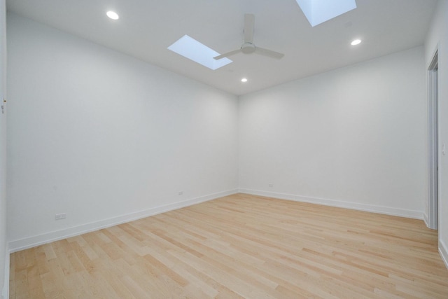 unfurnished room featuring light wood-style flooring, a skylight, a ceiling fan, and baseboards