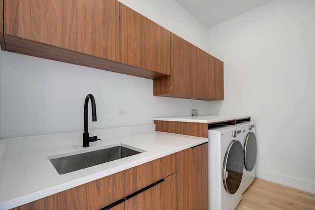 clothes washing area with cabinet space, light wood-style floors, a sink, separate washer and dryer, and baseboards