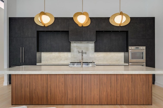 kitchen featuring appliances with stainless steel finishes, light wood-style floors, dark cabinets, and decorative backsplash