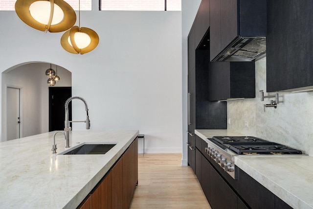 kitchen with arched walkways, hanging light fixtures, light wood-style floors, stainless steel gas cooktop, and a sink