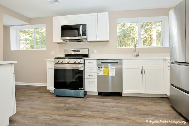 kitchen featuring appliances with stainless steel finishes, a wealth of natural light, light hardwood / wood-style floors, and white cabinets