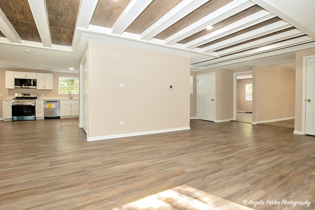 unfurnished living room featuring beam ceiling, sink, and light wood-type flooring