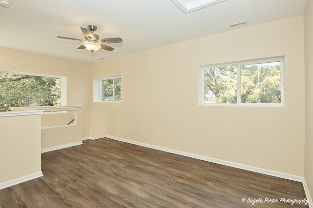 empty room featuring dark wood-type flooring, a skylight, a wealth of natural light, and ceiling fan