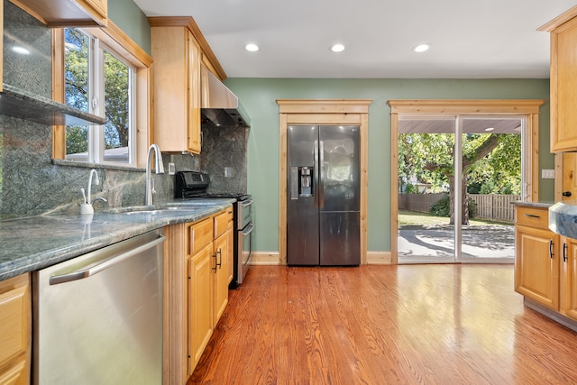 kitchen with appliances with stainless steel finishes, a healthy amount of sunlight, light hardwood / wood-style flooring, and tasteful backsplash