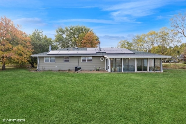 rear view of house featuring solar panels, a lawn, and a sunroom