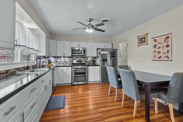 kitchen with white cabinetry, sink, stainless steel appliances, decorative backsplash, and light wood-type flooring