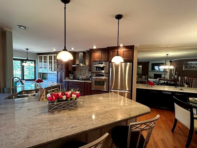 kitchen with sink, decorative light fixtures, wall chimney exhaust hood, hardwood / wood-style flooring, and stainless steel appliances