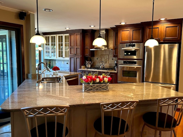 kitchen featuring wall chimney range hood, decorative backsplash, sink, stainless steel appliances, and hanging light fixtures