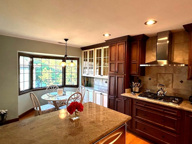 kitchen featuring light stone counters, hanging light fixtures, black gas cooktop, backsplash, and wall chimney range hood