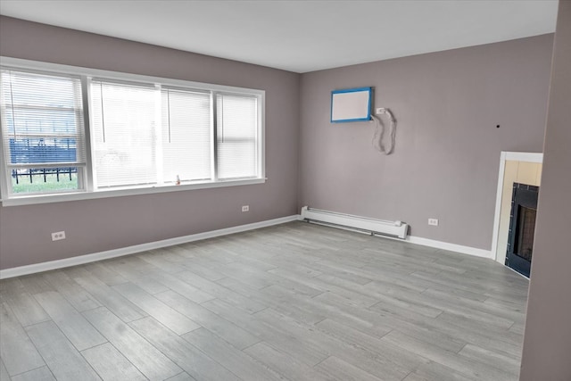 spare room with light hardwood / wood-style flooring, a fireplace, and a baseboard heating unit