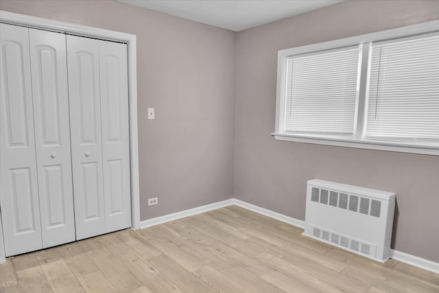 unfurnished bedroom with a closet, radiator, and light hardwood / wood-style floors