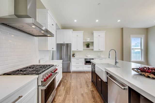 kitchen with wall chimney range hood, sink, white cabinets, and appliances with stainless steel finishes