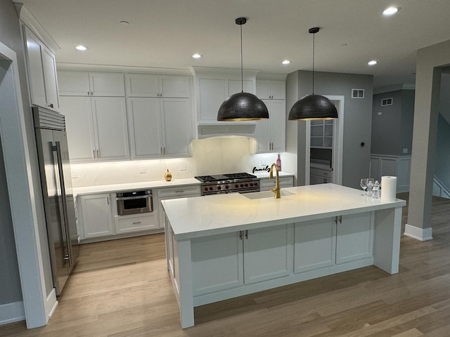 kitchen with a kitchen island with sink, sink, premium appliances, and white cabinets