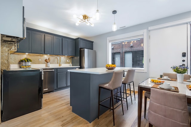 kitchen featuring light hardwood / wood-style floors, hanging light fixtures, stainless steel appliances, a kitchen bar, and decorative backsplash