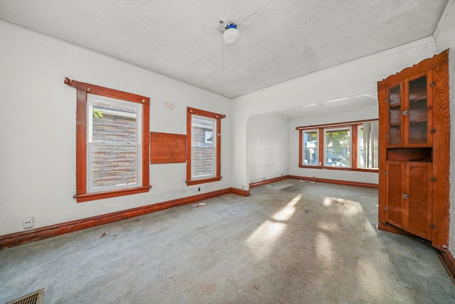 empty room with a textured ceiling, carpet floors, and crown molding