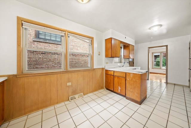 kitchen featuring wood walls, kitchen peninsula, light tile patterned floors, and sink