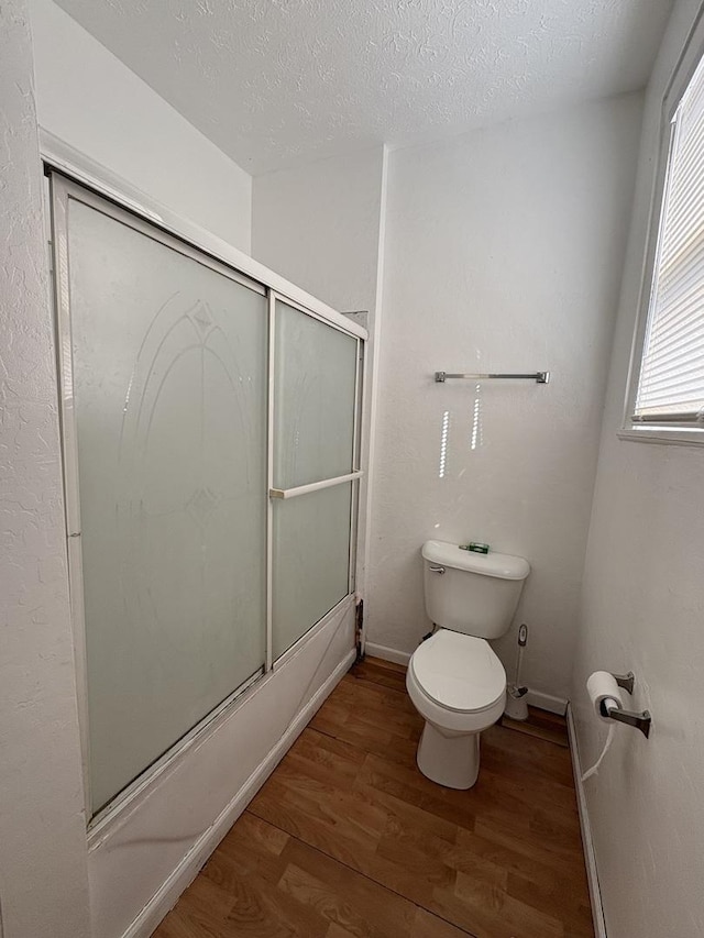 full bath with baseboards, a textured ceiling, toilet, bath / shower combo with glass door, and wood finished floors