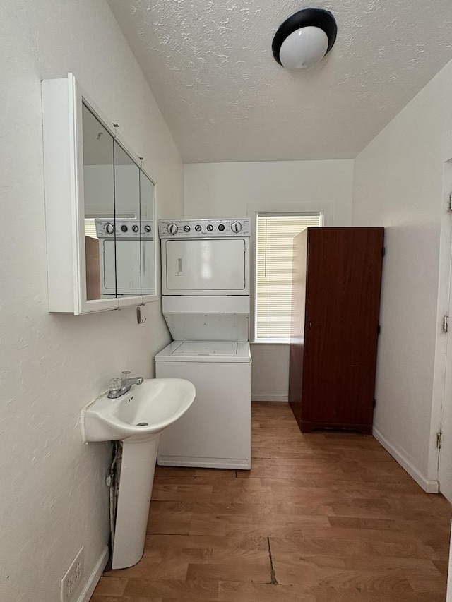 bathroom featuring a textured ceiling, stacked washer and dryer, wood finished floors, and baseboards