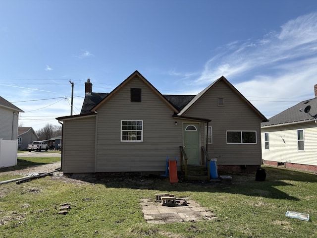 back of property featuring entry steps, roof with shingles, a yard, and a chimney