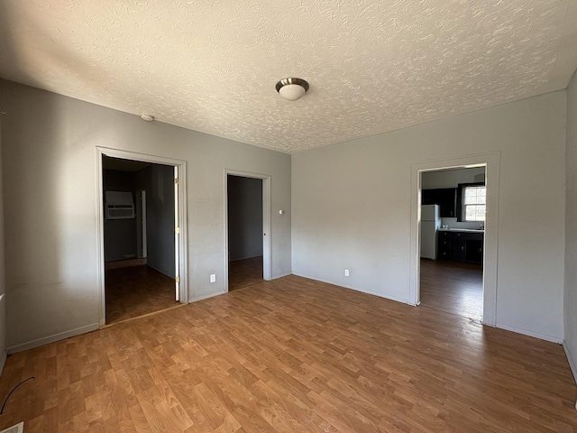 unfurnished bedroom featuring a textured ceiling, freestanding refrigerator, and wood finished floors