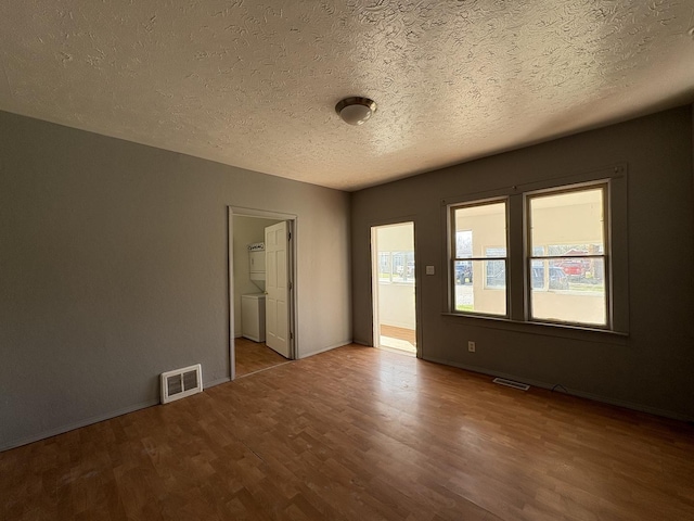 unfurnished room with a textured ceiling, wood finished floors, baseboards, and visible vents
