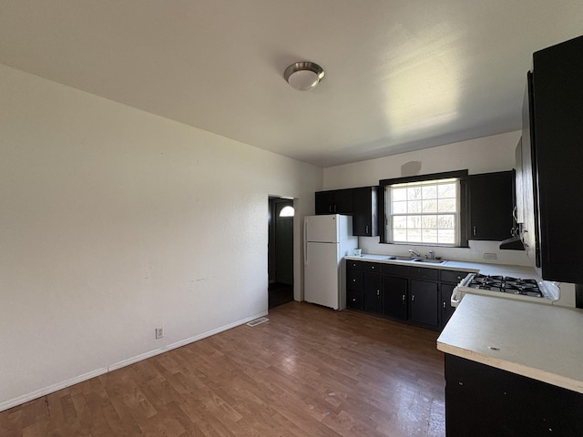 kitchen with white appliances, dark cabinets, wood finished floors, a sink, and light countertops