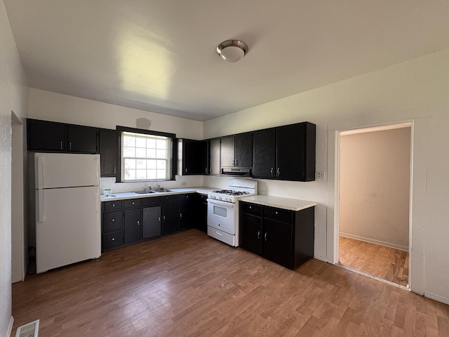 kitchen with visible vents, a sink, light countertops, white appliances, and dark cabinetry