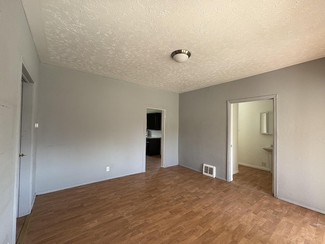 unfurnished bedroom with connected bathroom, a textured ceiling, visible vents, wood finished floors, and baseboards