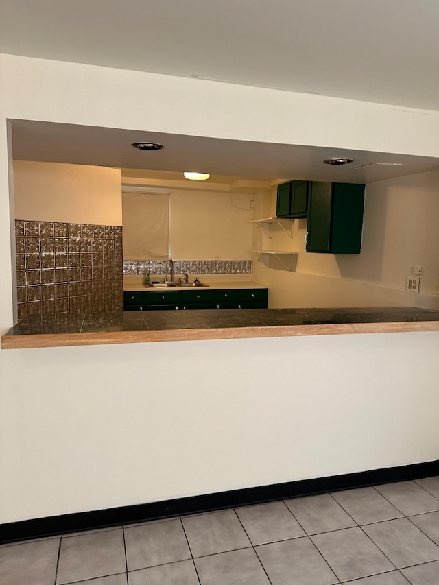 interior space featuring light tile patterned flooring, decorative backsplash, sink, and green cabinetry