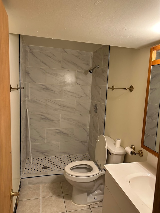 bathroom with vanity, a tile shower, toilet, and tile patterned floors