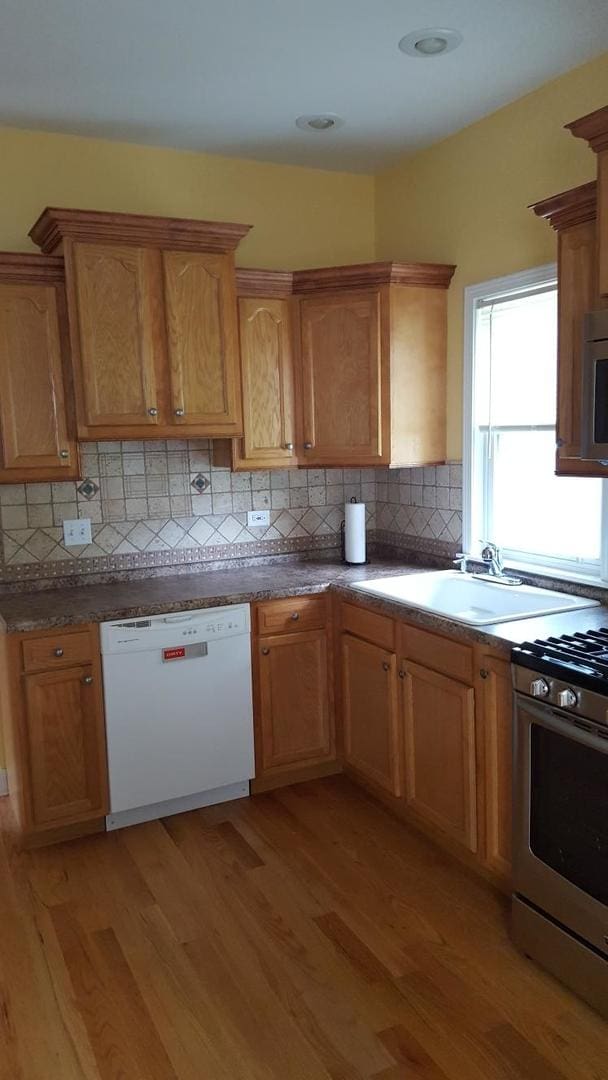 kitchen with appliances with stainless steel finishes, light hardwood / wood-style floors, sink, and tasteful backsplash