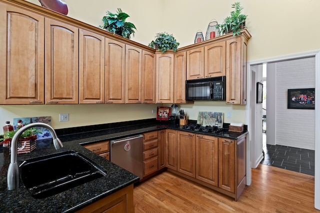 kitchen with dark stone counters, light wood-type flooring, black appliances, and sink