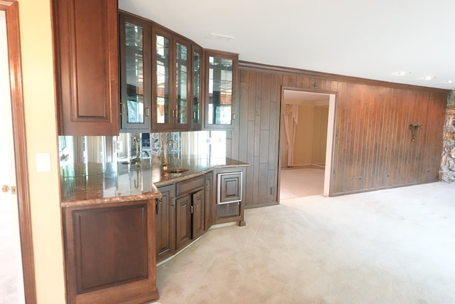 bar with sink, light colored carpet, stone counters, wooden walls, and ornamental molding