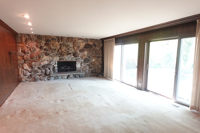 unfurnished living room featuring crown molding, a fireplace, wood walls, and light colored carpet