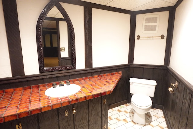 bathroom with a paneled ceiling, tile patterned flooring, vanity, and toilet