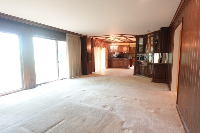 unfurnished living room with ornamental molding, wooden walls, a notable chandelier, and light carpet