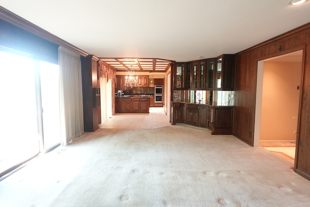 unfurnished living room with wooden walls, ornamental molding, a chandelier, and light colored carpet