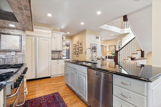 kitchen featuring sink, light hardwood / wood-style flooring, dark stone countertops, high end appliances, and an island with sink