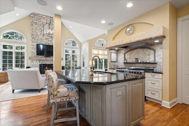 kitchen featuring sink, a kitchen breakfast bar, decorative backsplash, a stone fireplace, and light wood-type flooring