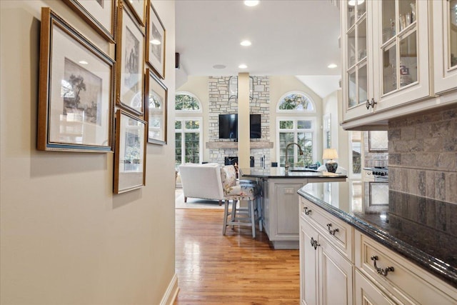 kitchen with a kitchen bar, dark stone counters, a fireplace, light hardwood / wood-style floors, and backsplash