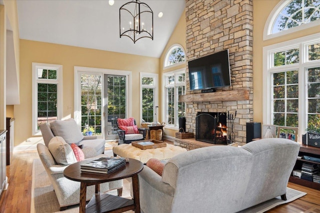 living room with a stone fireplace, a chandelier, high vaulted ceiling, and light wood-type flooring