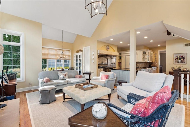 living room with high vaulted ceiling, a notable chandelier, and light wood-type flooring